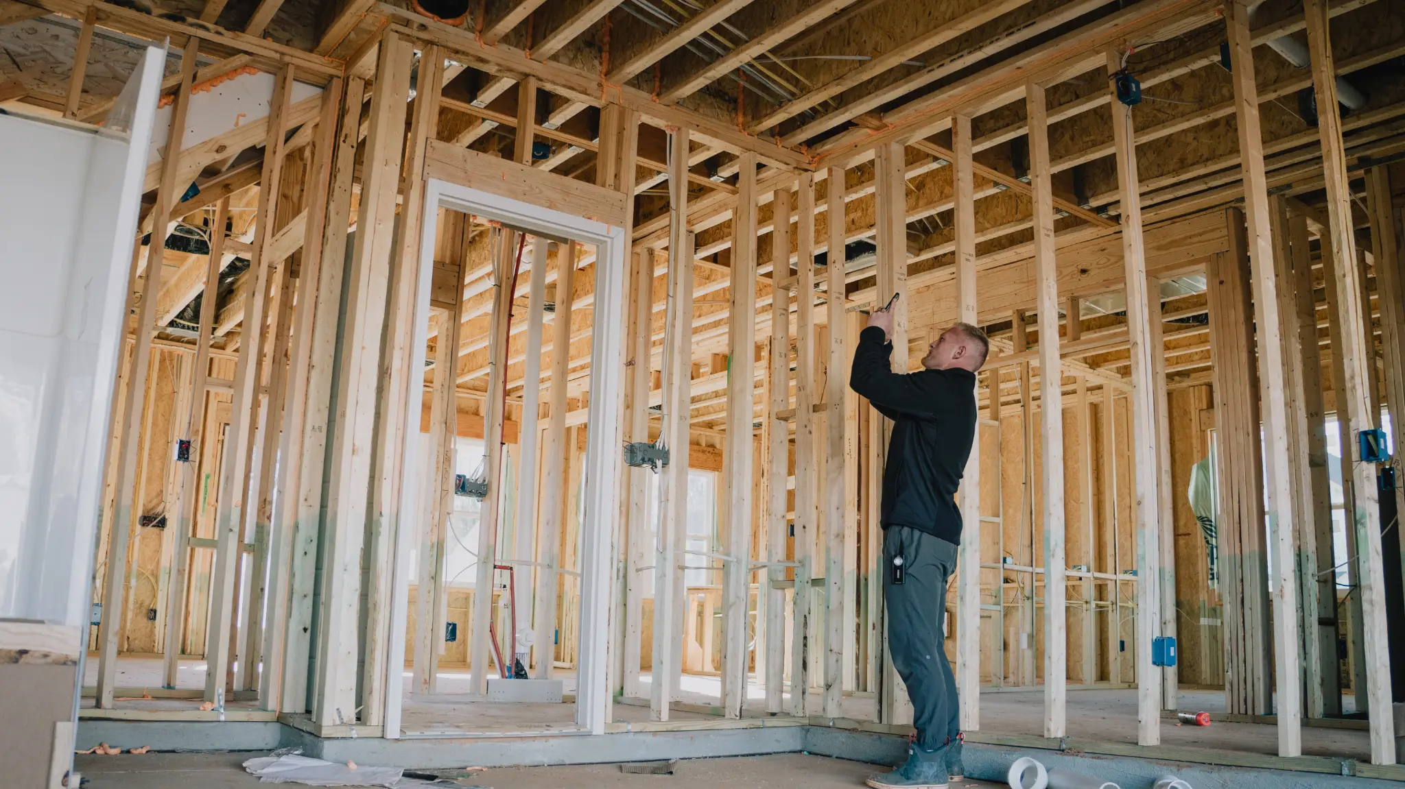 What First-Time Home Buyers Should Know About Inspections Person examining exposed wood framing inside an unfinished new-construction home before drywall installation.